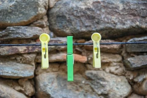 Colorful empty clothespins hanging on string front of stone wall background. Stock Photos