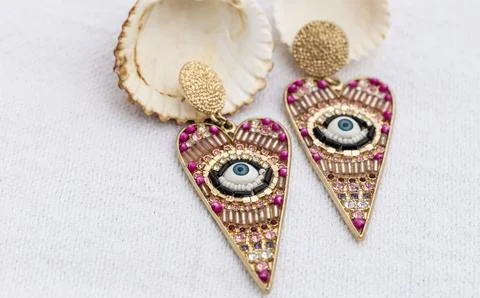 Colorful eye-patterned earrings with shells on white background, copy space. Foto stock