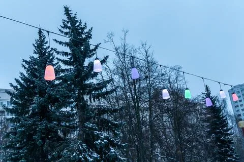 Colorful festive string lights line hanging over city street on winter day,.. Stock Photos