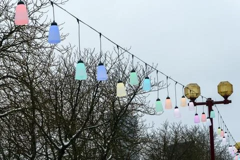 Colorful festive string lights line hanging over city street on winter day,.. Stock Photos