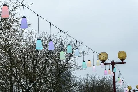 Colorful festive string lights line hanging over city street on winter day,.. 스톡 사진