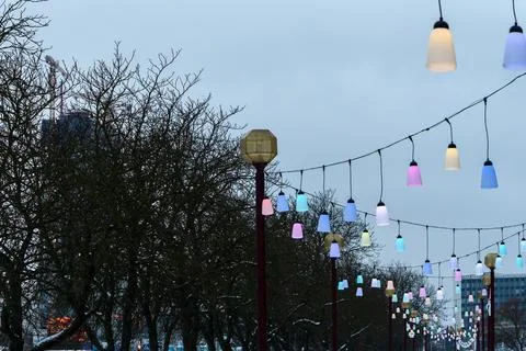 Colorful festive string lights line hanging over city street on winter day,.. Stock Photos