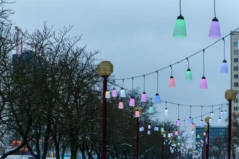 Colorful festive string lights line hanging over city street on winter day,.. Stock Photos