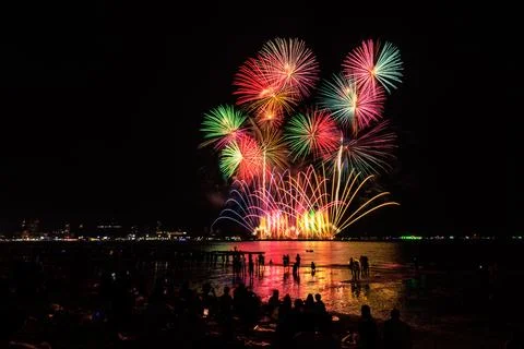 Colorful Fireworks Exploding Over Crowded Seaside Beach At Night Wide Shot Stock Photos
