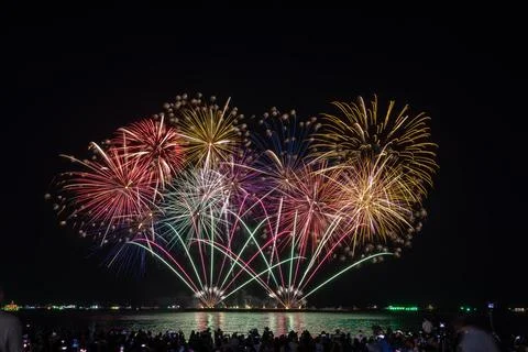 Colorful Fireworks Exploding Over The Water At Night With A Crowd Watching .. Stock Photos