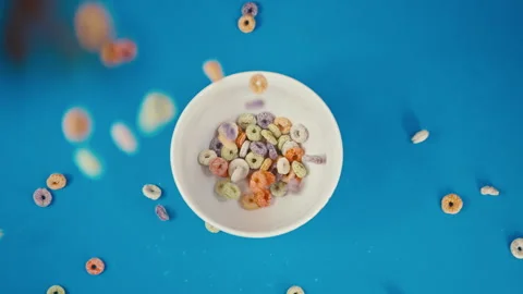 Colorful Fruit Cereal Loops Falling into Bowl on Blue Background Stock Footage 335895092