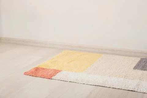 Colorful geometric patterned area rug on light wood floor with white wall and Stock Photos