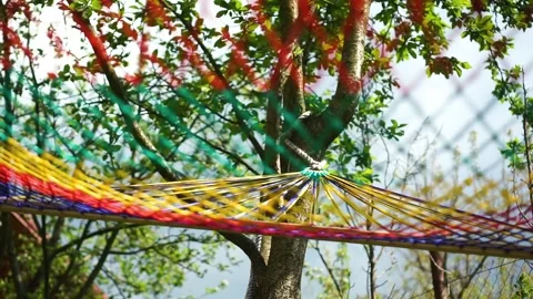 Colorful hammock net swinging back and forth tied to a tree. Summer time Vídeo Stock 243939417