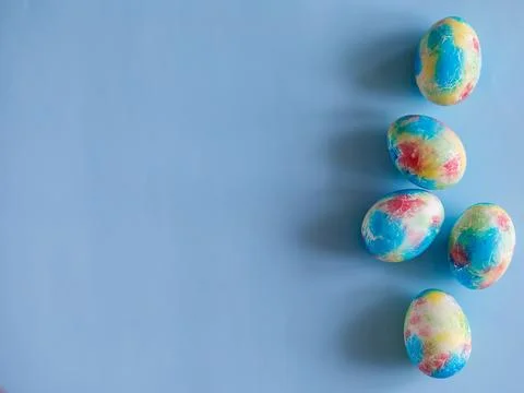 Colorful handmade Easter eggs painted like Earth on blue paper background with Stock Photos