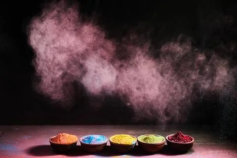 Colorful holi powder exploding from bowls on black background Stock Photos