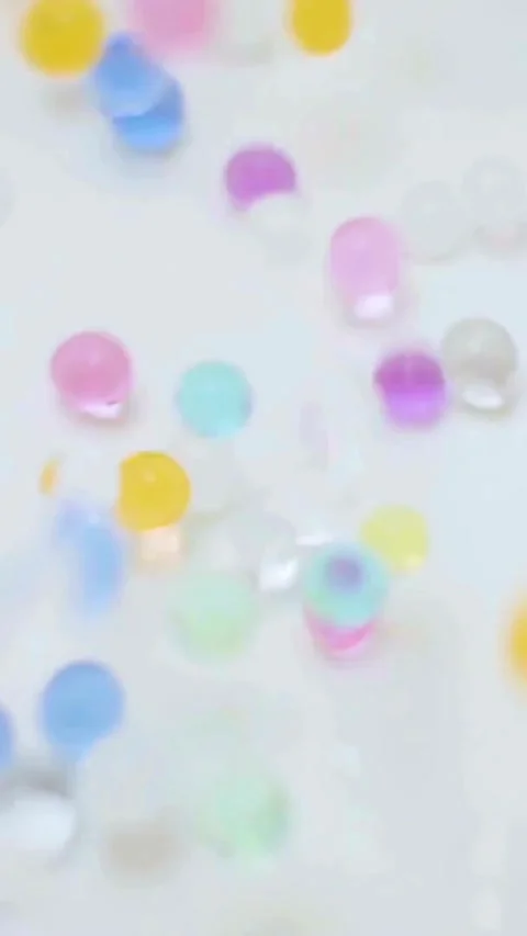 Colorful hydrogel beads falling on a white flat surface Stock Footage 334169807