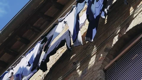 Colorful laundry hanging outside a rustic Italian building against blue skies Stock Footage 323953659
