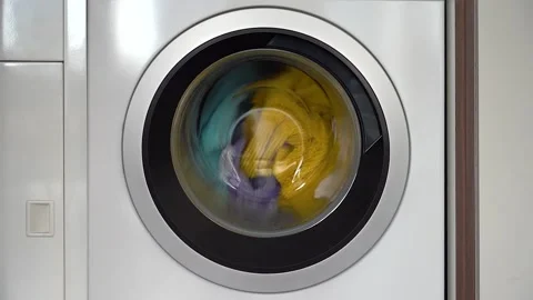 Colorful laundry inside a front loader washing machine spinning Stock Footage 195411788