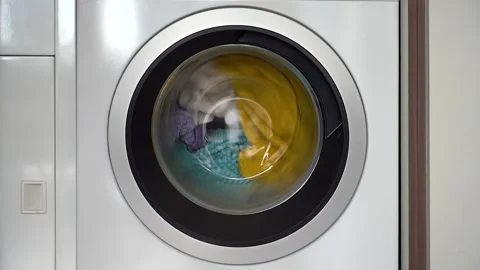 Colorful laundry inside a front loader washing machine spinning Stock Footage 197097354