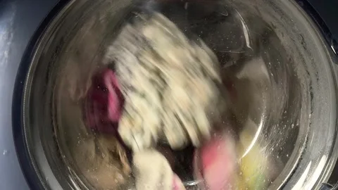 Colorful laundry spinning inside washing machine drum behind wet glass door Stock-Footage 342438233