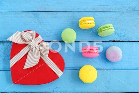 Colorful macaroni cookies and a heart-shaped box on a blue wooden vintage bac Stock Photos