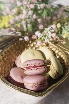 Colorful macarons are elegantly placed in a gold leaf bowl, accompanied by fr Stock Photos