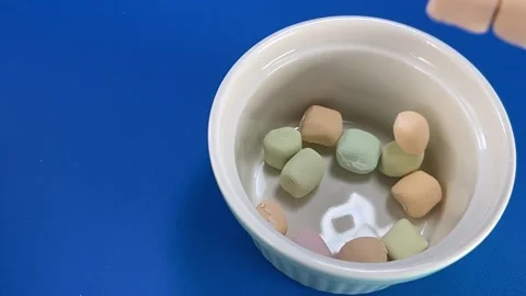 Colorful Marshmallows Falling Into White Bowl Against Blue Background Stock Footage 345274540