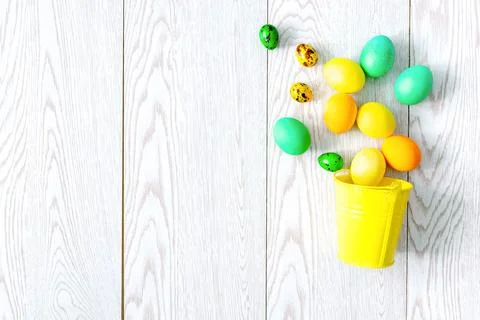 Colorful painted dye easter eggs lie in decor yellow bucket on wooden backg.. Stock Photos