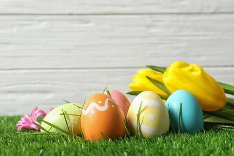 Colorful painted Easter eggs and flowers on green grass against wooden backgr Foto stock