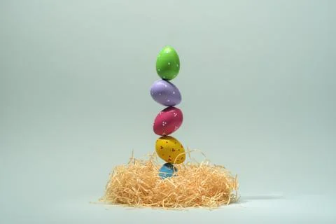 Colorful painted Easter eggs balance in tall stack on straw nest against soft 스톡 사진