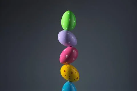 Colorful painted Easter eggs balance in vertical stack against dark gray Stock Photos
