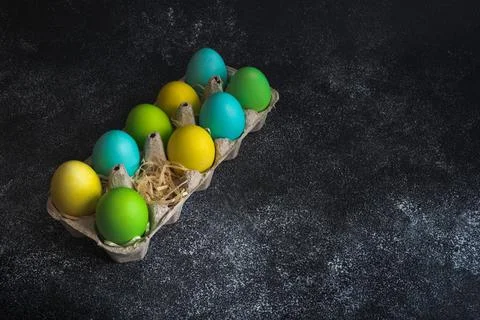 Colorful painted easter eggs in egg carton decorated with shavings on black Stock Photos