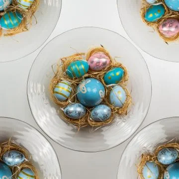 Colorful painted easter eggs in straw nest in a circular glass bowl Stock Photos