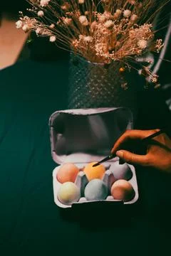 Colorful painted Easter eggs in a violet box, a paint brush in woman's hands Stock Photos
