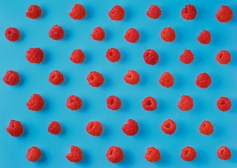 Colorful pattern of ripe raspberry berries on a bright blue background. Stock Photos
