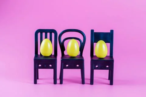 Colorful Plastic Easter Eggs on small chairs on pink background Stock-Fotos
