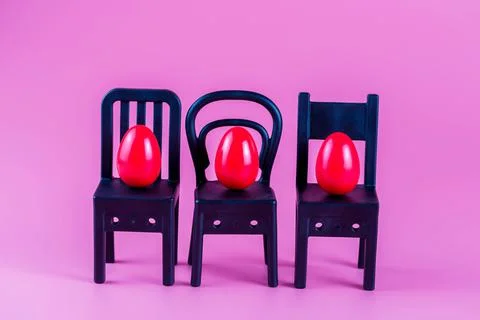 Colorful Plastic Easter Eggs on small chairs on pink background Stock Photos