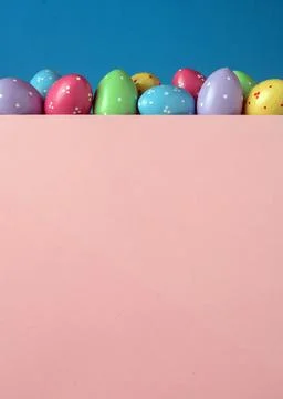 Colorful polka dot Easter eggs peek over pink board on blue background, playf Stock Photos
