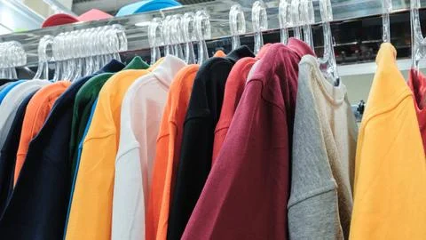 Colorful pullover sweaters hang on clear plastic hangers. Orange, red, black, Фото