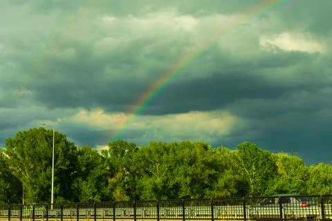 Colorful rainbow against the backdrop of thunderclouds, clouds over the forest Stock Photos