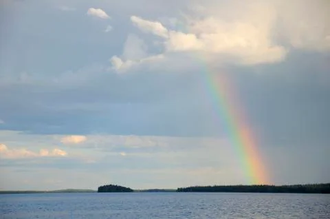 Colorful rainbow under single cloud over lake Stock Photos