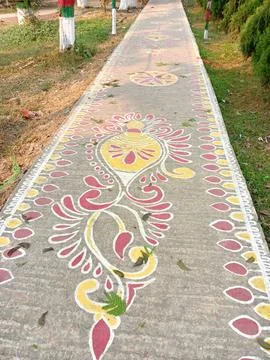 Colorful rangoli art designed on a pathway surrounded by greenery and trees Stock Photos