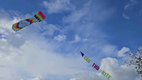 A colorful, rectangular kite soars gracefully against a bright blue sky clouds. 스톡 동영상 302772489