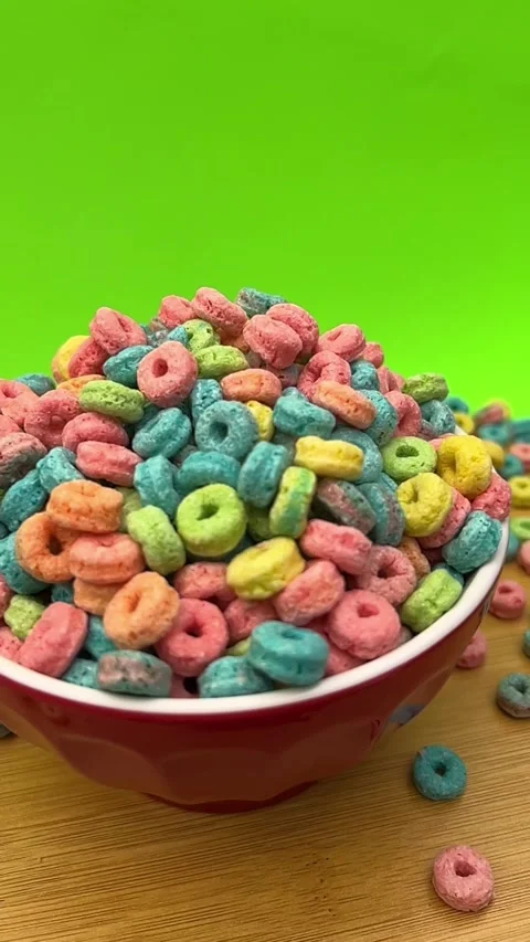 Colorful Ring Shaped Cereal Pieces in Bowl Against Bright Green Background Stock Footage 345365525