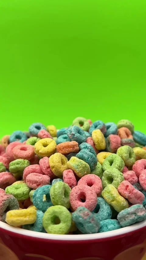 Colorful Ring Shaped Cereal in Red Bowl Against Bright Green Background Stock Footage 344500057