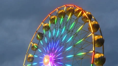 Colorful rotating nostalgic Ferris Wheel - dark cloudy sky - real time Stock Footage 140739718