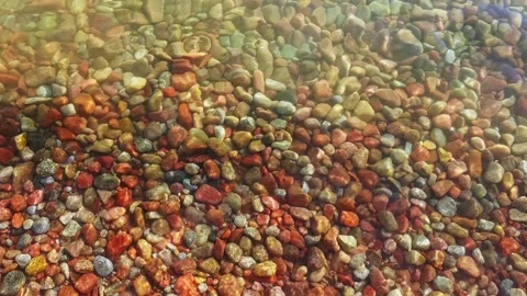 Colorful round rocks at the beach lit by sun light through thin layer of water Stock Footage 303533940