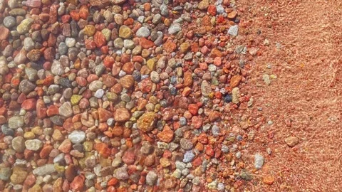 Colorful round rocks at the beach lit by sun light through thin layer of water Stock Footage 303534663