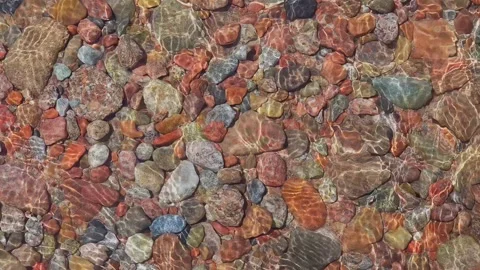 Colorful round rocks at the beach lit by sun light through thin layer of water Stock Footage 303592698