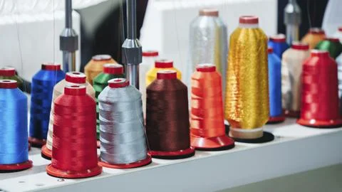 Colorful sewing thread spools line white shelf. Spools feature bright hues li 写真素材