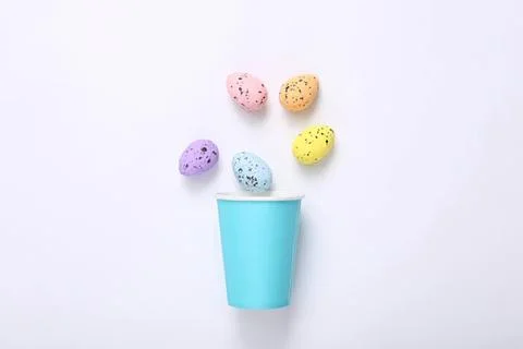 Colorful speckled eggs falling into a blue cup on white background Stock Photos