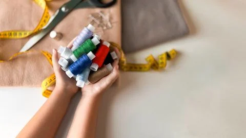 Colorful spools of thread in hands with sewing supplies on table Stock-Fotos