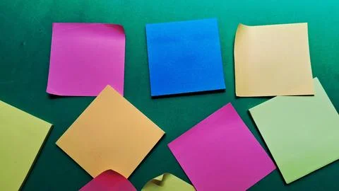 Colorful square sticky notes arranged randomly on a dark green background Stock Photos