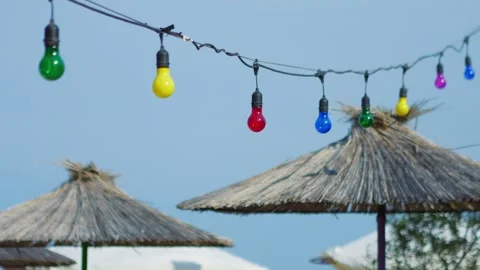 Colorful string lights hanging above straw umbrellas at a beach, evoking a .. Stock Footage 293087068