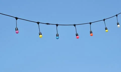 Colorful string lights hanging against clear blue sky with copy space Stock Photos
